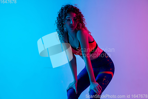 Image of Portrait of young beautiful woman in bright sportwear isolated on gradient pink-blue studio background in neon light.