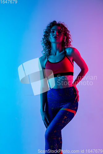 Image of Portrait of young beautiful woman in bright sportwear isolated on gradient pink-blue studio background in neon light.