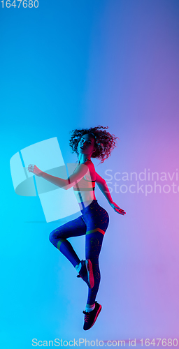 Image of Portrait of young beautiful woman in bright sportwear isolated on gradient pink-blue studio background in neon light.