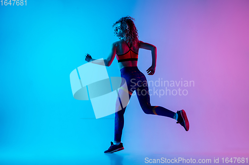 Image of Young sportive woman running isolated on gradient pink-blue studio background in neon light.