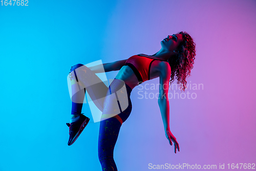 Image of Portrait of young beautiful woman in bright sportwear isolated on gradient pink-blue studio background in neon light.