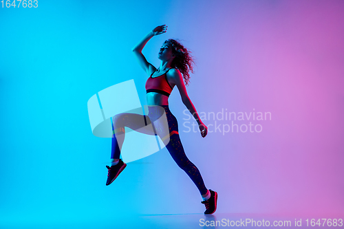 Image of Young sportive woman running isolated on gradient pink-blue studio background in neon light.