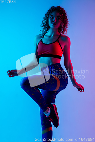 Image of Young sportive woman training isolated on gradient pink-blue studio background in neon light.