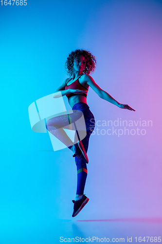 Image of Portrait of young beautiful woman in bright sportwear isolated on gradient pink-blue studio background in neon light.
