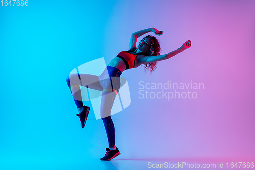 Image of Sportive young happy woman in bright sportwear isolated on gradient pink-blue studio background in neon light.