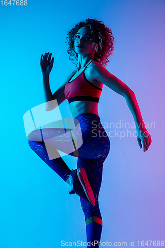 Image of Young sportive woman training isolated on gradient pink-blue studio background in neon light.