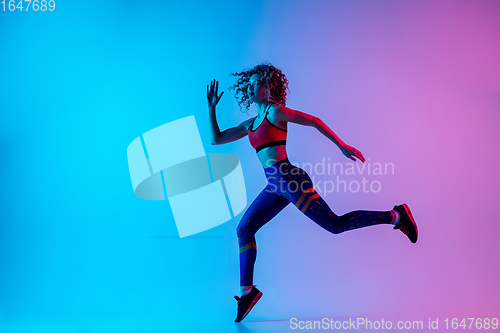 Image of Young sportive woman running isolated on gradient pink-blue studio background in neon light.