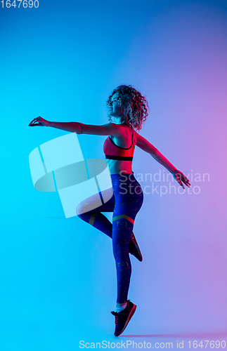 Image of Young sportive woman training isolated on gradient pink-blue studio background in neon light.