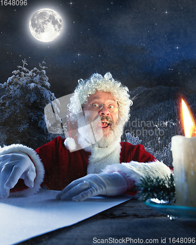 Image of Emotional Santa Claus congratulating with New Year and Christmas, writing a letter, wish list in midnight with candle