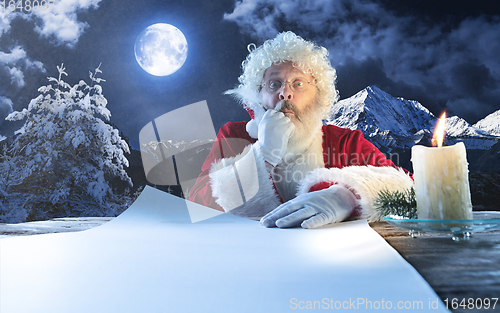 Image of Emotional Santa Claus congratulating with New Year and Christmas, writing a letter, wish list in midnight with candle