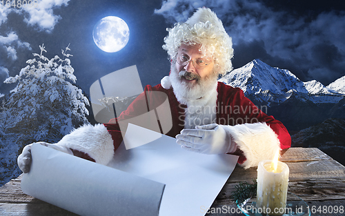 Image of Emotional Santa Claus congratulating with New Year and Christmas, writing a letter, wish list in midnight with candle