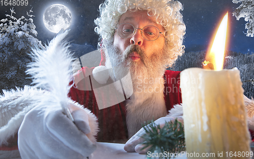 Image of Emotional Santa Claus congratulating with New Year and Christmas, writing a letter, wish list in midnight with candle