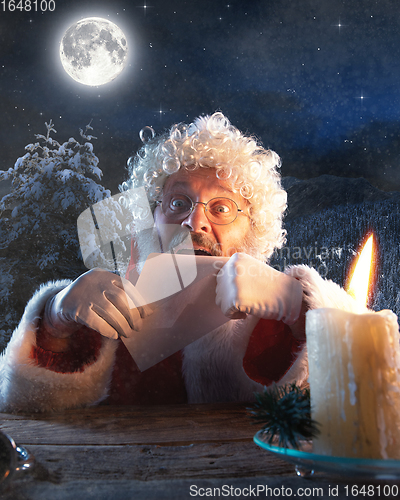 Image of Emotional Santa Claus congratulating with New Year and Christmas, sending a letter, wish list in midnight with candle