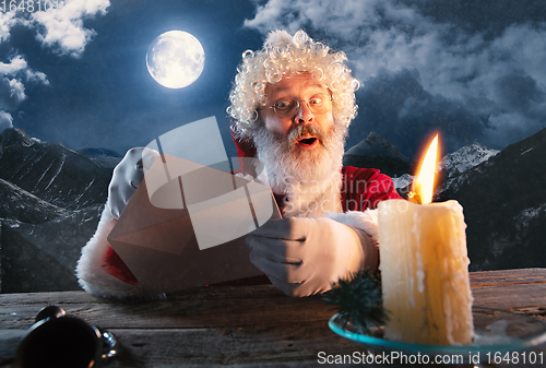 Image of Emotional Santa Claus congratulating with New Year and Christmas, sending a letter, wish list in midnight with candle