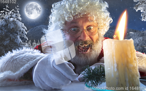 Image of Close-up portrait of emotional Santa Claus writing a letter,wish list with New Year and Christmas in midnight with candle