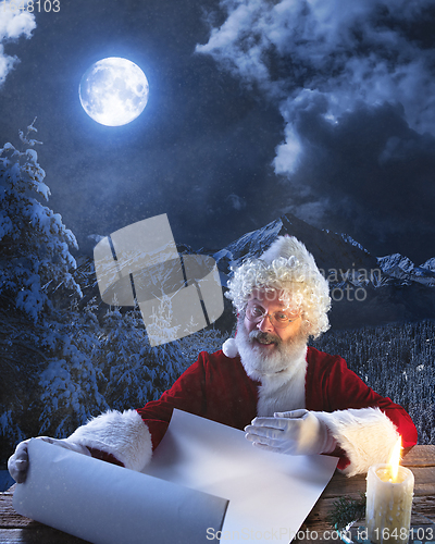 Image of Emotional Santa Claus congratulating with New Year and Christmas, writing a letter, wish list in midnight with candle