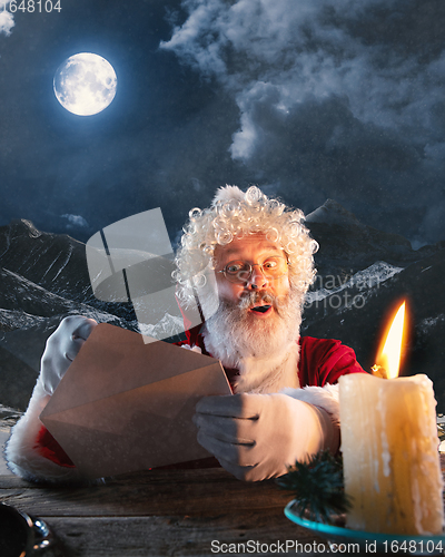 Image of Emotional Santa Claus congratulating with New Year and Christmas, sending a letter, wish list in midnight with candle