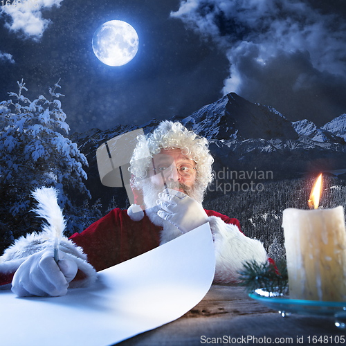 Image of Emotional Santa Claus congratulating with New Year and Christmas, writing a letter, wish list in midnight with candle