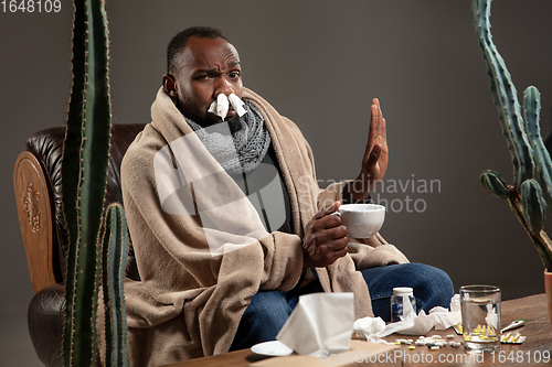 Image of Young African-American man wrapped in a plaid sitting at home trying to protect from somebody\'s sick