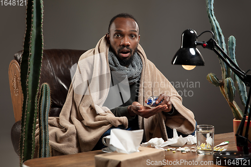 Image of Young African-american man wrapped in a plaid looks sick, ill sitting at home indoors.