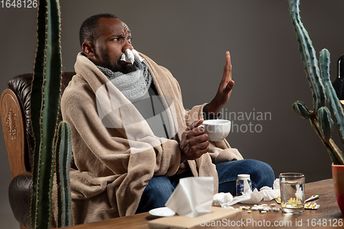 Image of Young African-American man wrapped in a plaid sitting at home trying to protect from somebody\'s sick