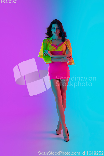 Image of Beautiful seductive girl in fashionable crimson and yellow outfit on bright gradient pink-blue background in neon light