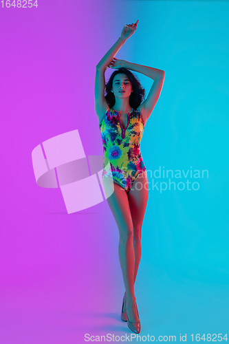 Image of Beautiful seductive girl in fashionable bright swimsuit on colour gradient pink-blue background in neon light.