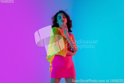 Image of Portrait of beautiful seductive girl in fashionable bright outfit on colour gradient pink-blue background in neon light.