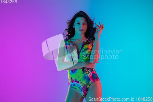 Image of Beautiful seductive girl in fashionable bright swimsuit on colour gradient pink-blue background in neon light.