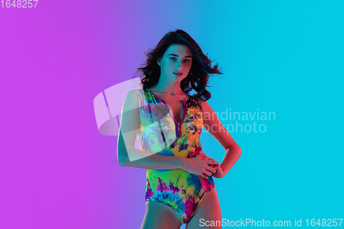 Image of Beautiful seductive girl in fashionable bright swimsuit on colour gradient pink-blue background in neon light.