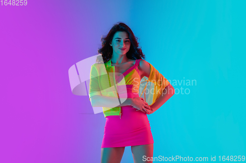 Image of Portrait of beautiful seductive girl in fashionable bright outfit on colour gradient pink-blue background in neon light.