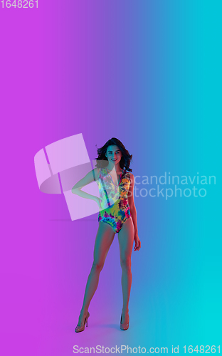 Image of Beautiful seductive girl in fashionable bright swimsuit on colour gradient pink-blue background in neon light.