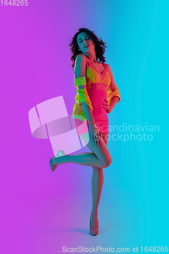 Image of Beautiful seductive girl in fashionable crimson and yellow outfit on bright gradient pink-blue background in neon light