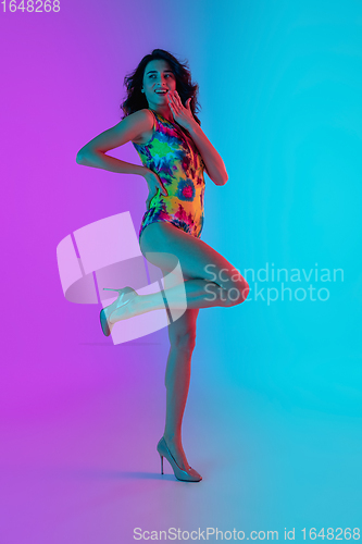 Image of Beautiful seductive girl in fashionable bright swimsuit on colour gradient pink-blue background in neon light.