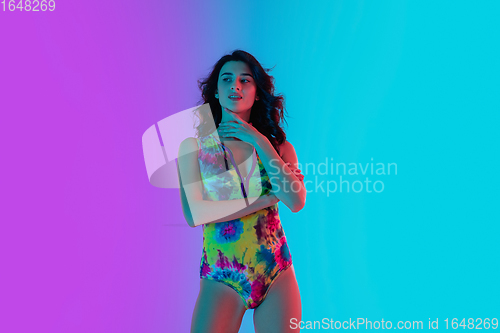 Image of Beautiful seductive girl in fashionable bright swimsuit on colour gradient pink-blue background in neon light.