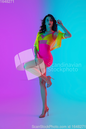 Image of Beautiful seductive girl in fashionable crimson and yellow outfit on bright gradient pink-blue background in neon light