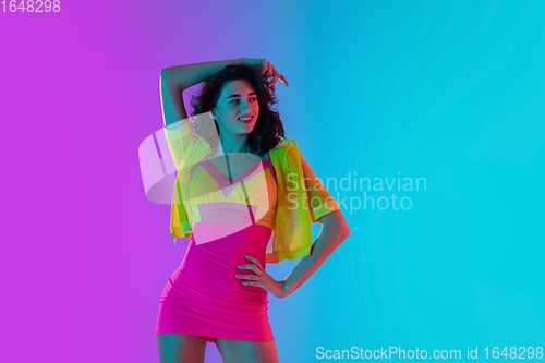 Image of Portrait of beautiful seductive girl in fashionable bright outfit on colour gradient pink-blue background in neon light.