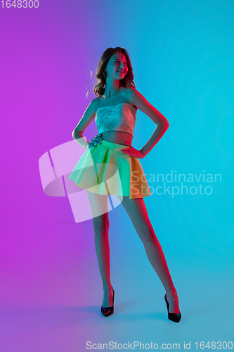 Image of Beautiful seductive girl in fashionable bright outfit posing on colour gradient pink-blue background in neon light.