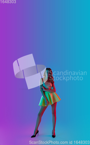 Image of Beautiful seductive girl in fashionable bright outfit posing on colour gradient pink-blue background in neon light.