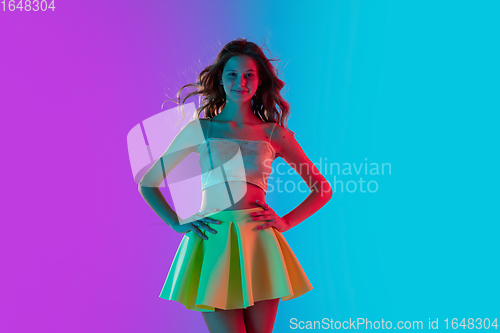 Image of Beautiful seductive girl in fashionable bright outfit posing on colour gradient pink-blue background in neon light.