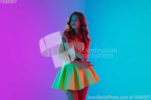 Image of Beautiful seductive girl in fashionable bright outfit posing on colour gradient pink-blue background in neon light.