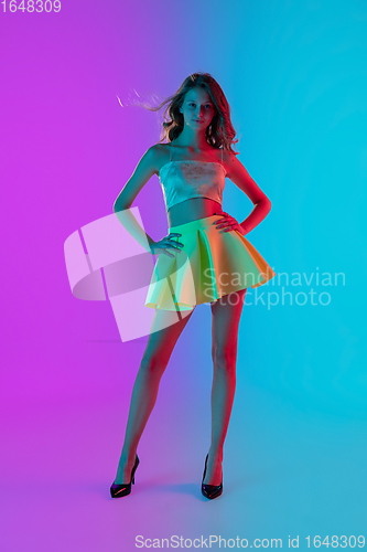 Image of Beautiful seductive girl in fashionable bright outfit posing on colour gradient pink-blue background in neon light.