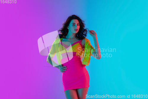 Image of Portrait of beautiful seductive girl in fashionable bright outfit on colour gradient pink-blue background in neon light.