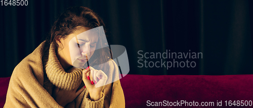 Image of Woman wrapped in a plaid looks sick, ill, sneezing and coughing sitting at home indoors