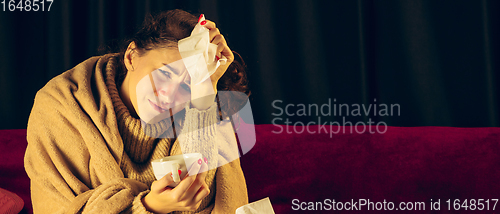 Image of Woman wrapped in a plaid looks sick, ill, sneezing and coughing sitting at home indoors