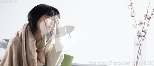 Image of Woman wrapped in a plaid looks sick, ill, sneezing and coughing sitting at home indoors