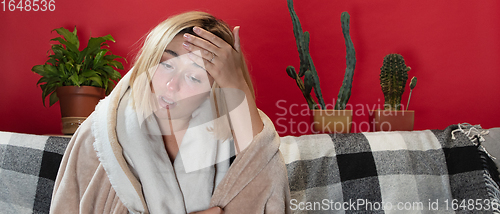Image of Woman wrapped in a plaid looks sick, ill, sneezing and coughing sitting at home indoors