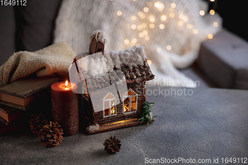 Image of Winter house miniature illuminated and books on grey and white background. The concept of home atmosphere and comfort.