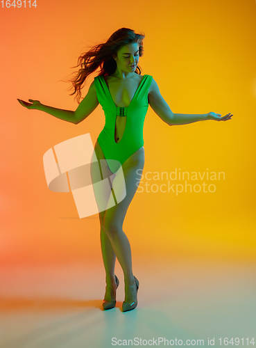 Image of Full-length portrait of beautiful seductive girl in fashionable green swimsuit on bright gradient background in neon light