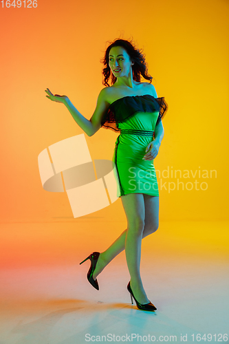 Image of Beautiful seductive girl in fashionable, modern outfit on bright gradient yellow-orange background in neon light
